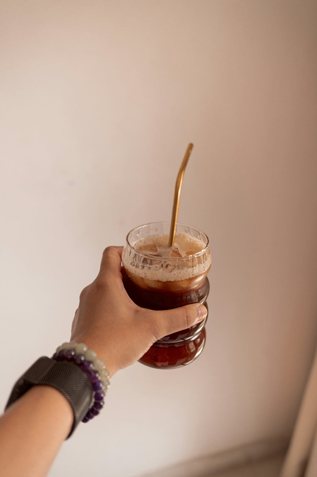 Hand holds a glass of iced coffee with a straw.