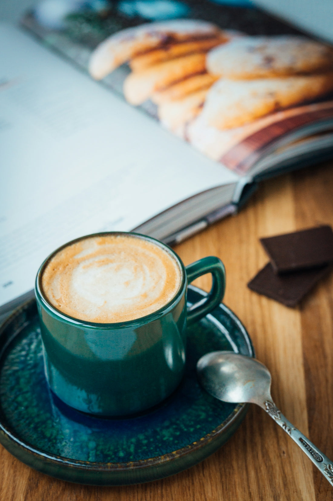 green ceramic mug with coffee beside silver spoon on brown wooden table