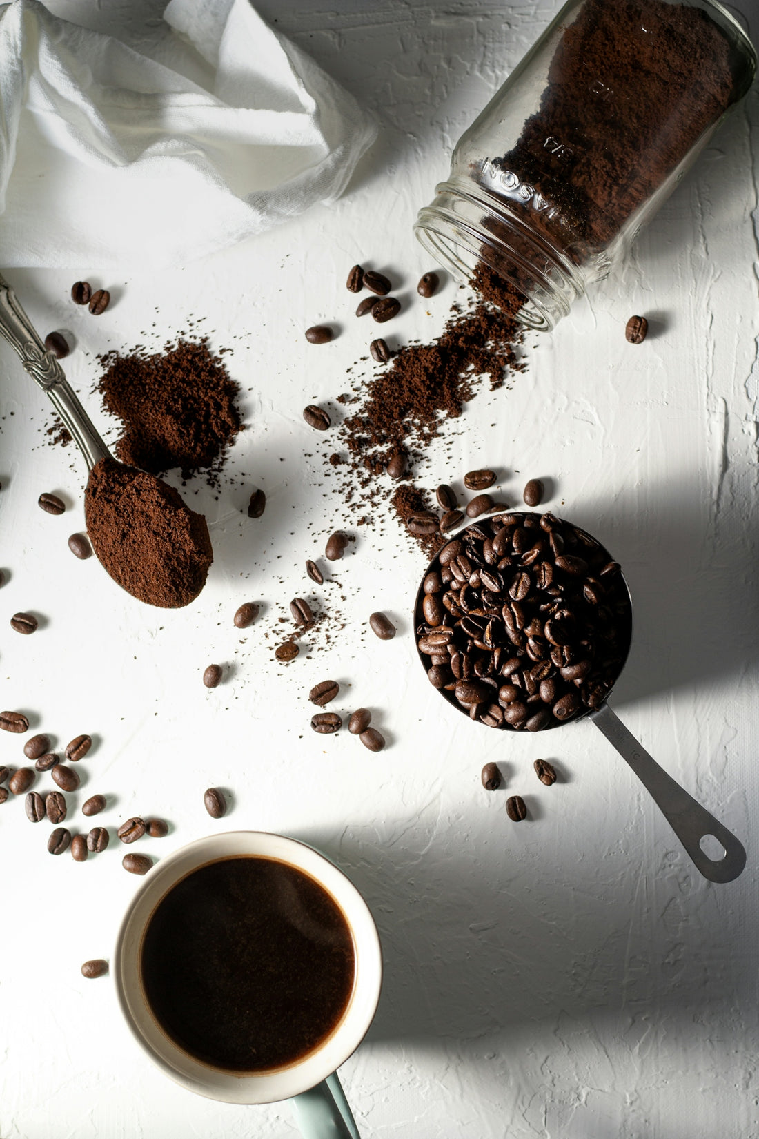 Coffee beans, ground coffee, and a cup of black coffee on a white surface