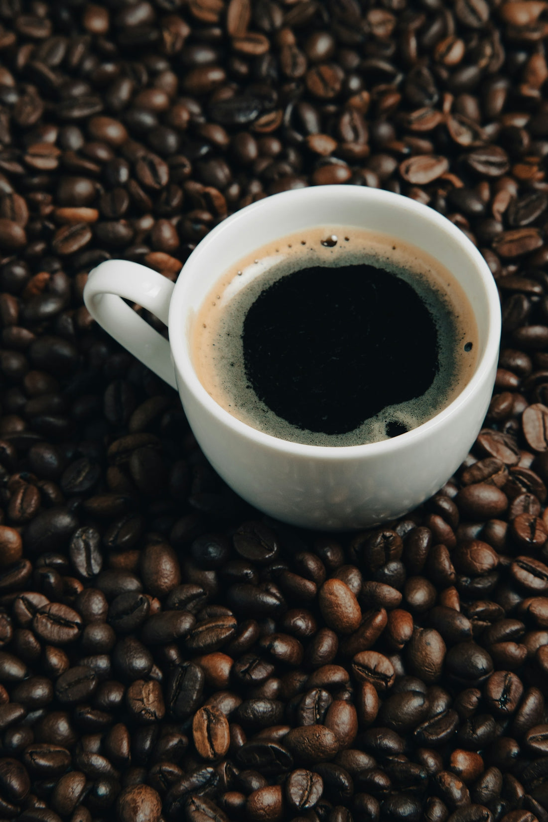 a cup of coffee sitting on top of a pile of coffee beans